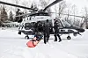 Politihelikopter på snødekket slette mens mannskap laster inn person på båre.