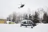 To politihelikoptre, ett på bakken og ett i lufta, over snødekt område med trær.
