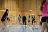 Ungdommer spiller håndball i idrettshall mens en voksen trener følger med fra midten av banen.