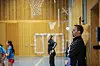 Mann i treningsklær står ved veggen og ser på håndballtrening i en idrettshall.