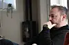 Mann sitter i sofaen hjemme, i profil, og ser tankefull ut med hånden mot ansiktet.