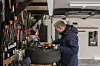 Mann i jakke arbeider ved arbeidsbenk i garasje med mange verktøy på veggen.