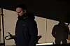 Mann i mørk jakke står alene i skarpt lys i en garasje med tydelig skygge på veggen.