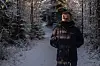 Mann med mørk jakke står på snødekt skogssti omgitt av vintertrær.