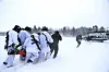 Soldater i hvite vinterklær bærer en båre mot et helikopter i snødekt landskap.