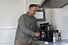 En mann står ved en kaffemaskin på et lyst kjøkken og fyller en kopp.