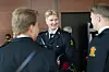 Tre personer i mørke uniformer står i en innendørs lobby og snakker sammen.