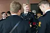 Flere uniformerte personer står i samtale innendørs, med en mann som holder røde roser i forgrunnen.