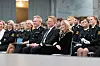 En gruppe politistudenter i uniform sitter på stoler under en seremoni innendørs.