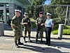 Fire uniformerte personer står utenfor et gjerde ved en bygning med flagg.