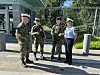 Fire uniformerte personer står utenfor et gjerde ved en bygning med flagg.