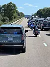 Politibil og motorsykler med blålys kjører foran en lang bilkortesje på en motorvei.