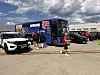 En blå norsk landslagsbuss står parkert ved en bygning med flere biler og personer rundt.