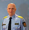 En mann i politiuniform står foran en blå vegg med politilogoer.