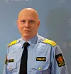 En mann i politiuniform står foran en blå vegg med politilogoer.