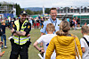 Politifolk i refleksvester står og snakker med flere tilskuere på en fotballarena.