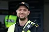 En smilende politiansatt i uniform med sambandsradio står foran en bygning.