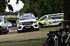 Tre politibiler står parkert på en gresslette ved trær og boligblokker, med sykler i forgrunnen.