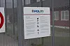 Et hvitt politiskilt med logo og informasjon står bak et metallgjerde.