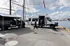 Tre store kjøretøy står parkert på en kai ved Oslofjorden, med seilbåtmaster og bybildet i bakgrunnen.